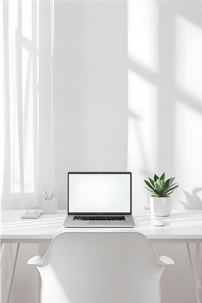 Minimalist white home office desk with a white chair, small potted plant, laptop, and clean desk accessories in a bright room.